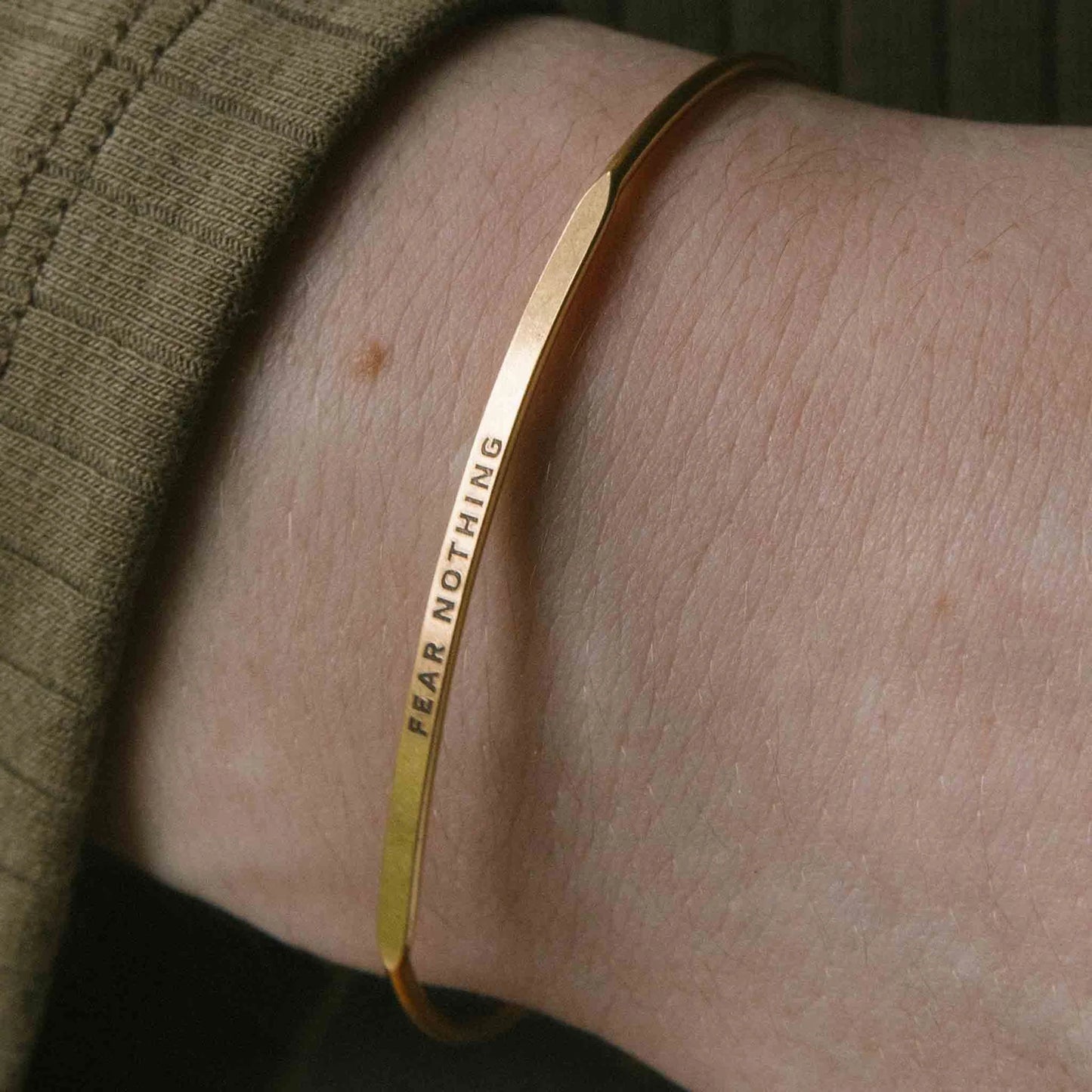Gold bracelet with 'FEAR NOTHING' engraving on a wrist.
