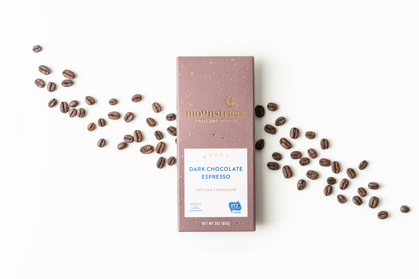Moonstruck Dark Chocolate Espresso bar with scattered coffee beans on a white background