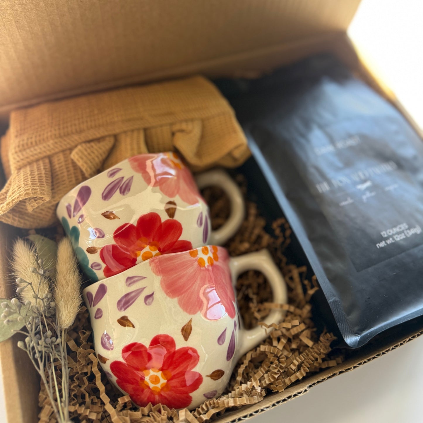 Floral mug with a box labeled 'The Fox and Pantry' containing tea bags and a small plant.