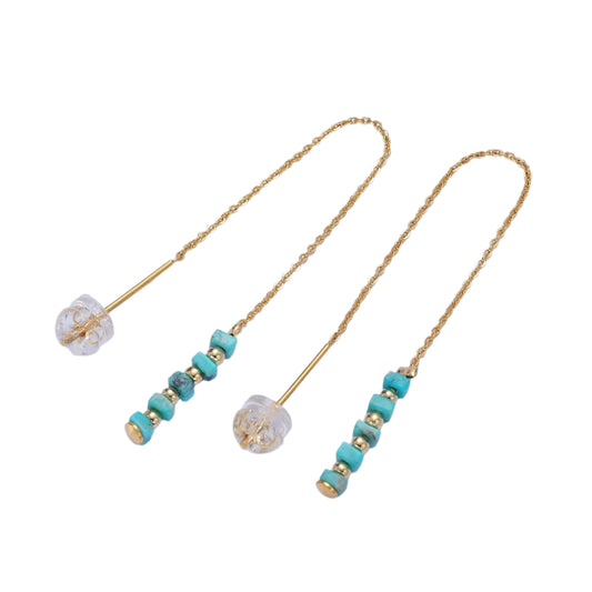 Pair of earrings with turquoise beads and gold chains on a light blue background