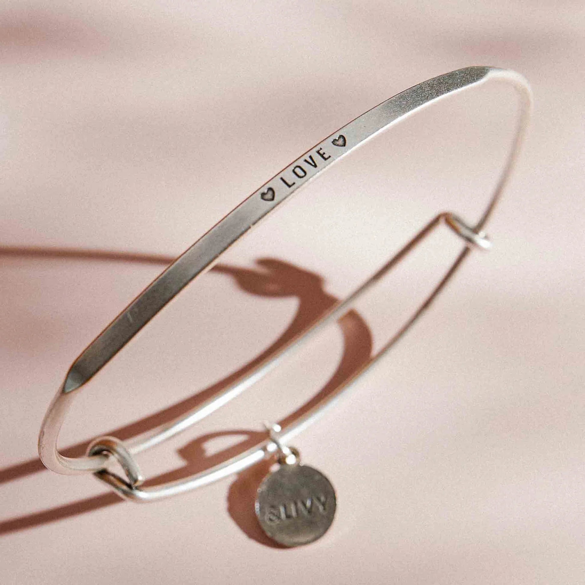 Silver bracelet with 'LOVE' and heart symbols on a pink background