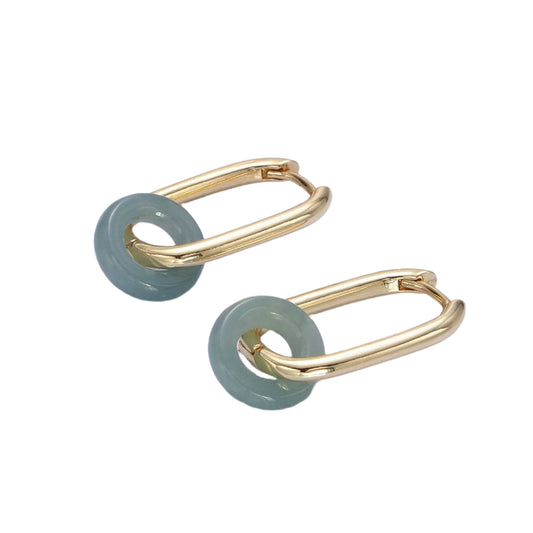Gold hoop earrings with green jade-like stones on a light purple background
