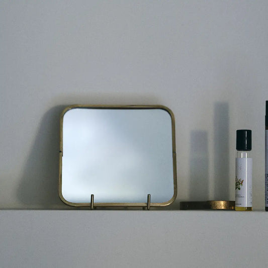Rectangular mirror with brass frame on a white surface with a minimal background