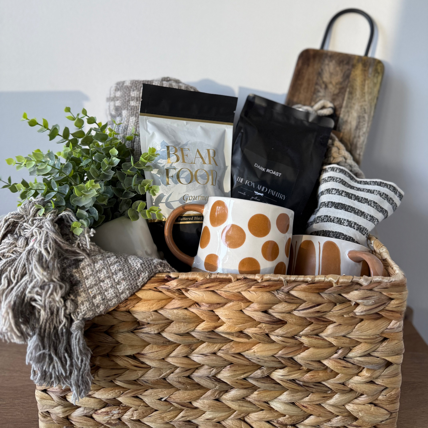Woven basket with coffee, cups, and a plant on a neutral background