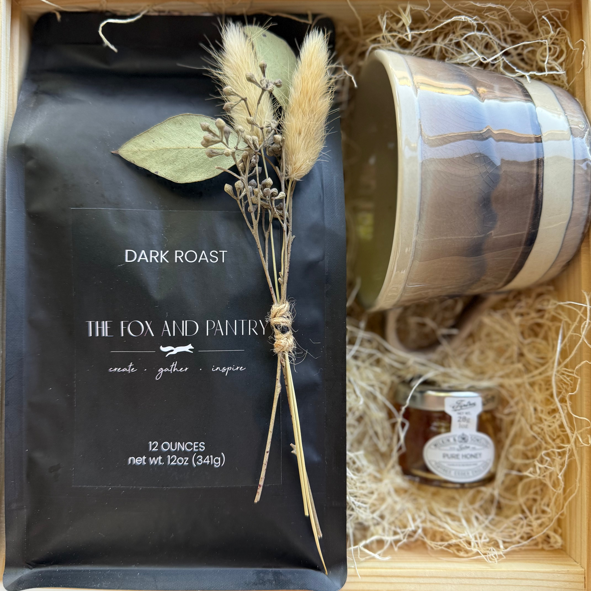 Gift set with coffee package, ceramic mug, and jar of honey in a wooden box.