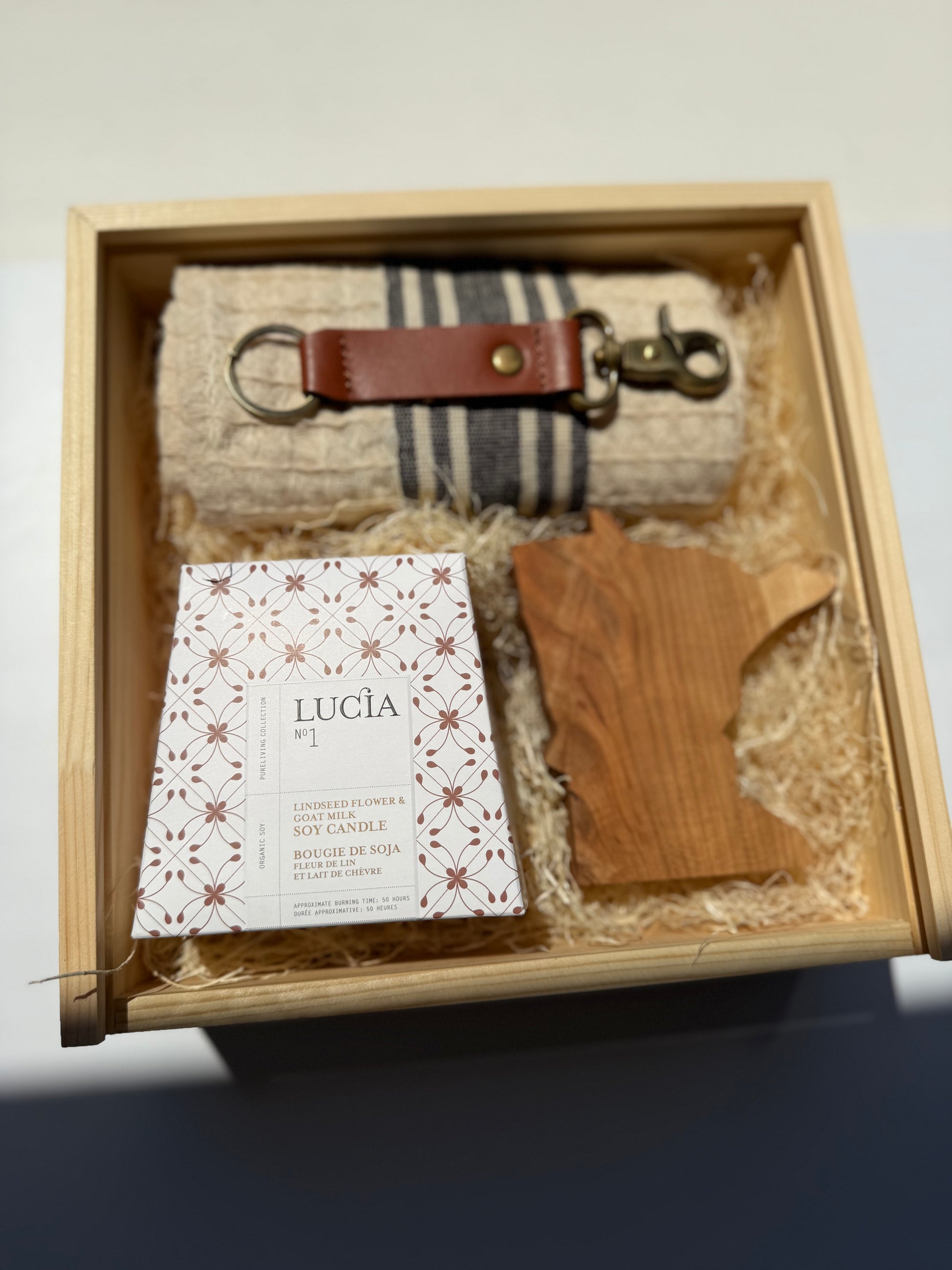 Gift set with a keychain, towel, and wooden item in a box, featuring the brand 'Lucia'.