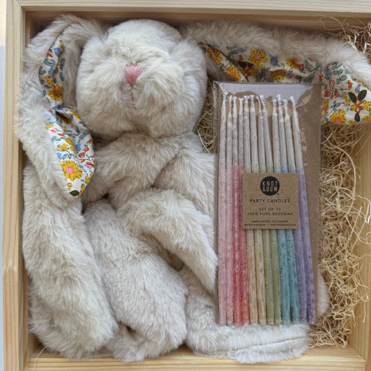 Plush bunny toy with colorful candles and decorative items in a wooden box.