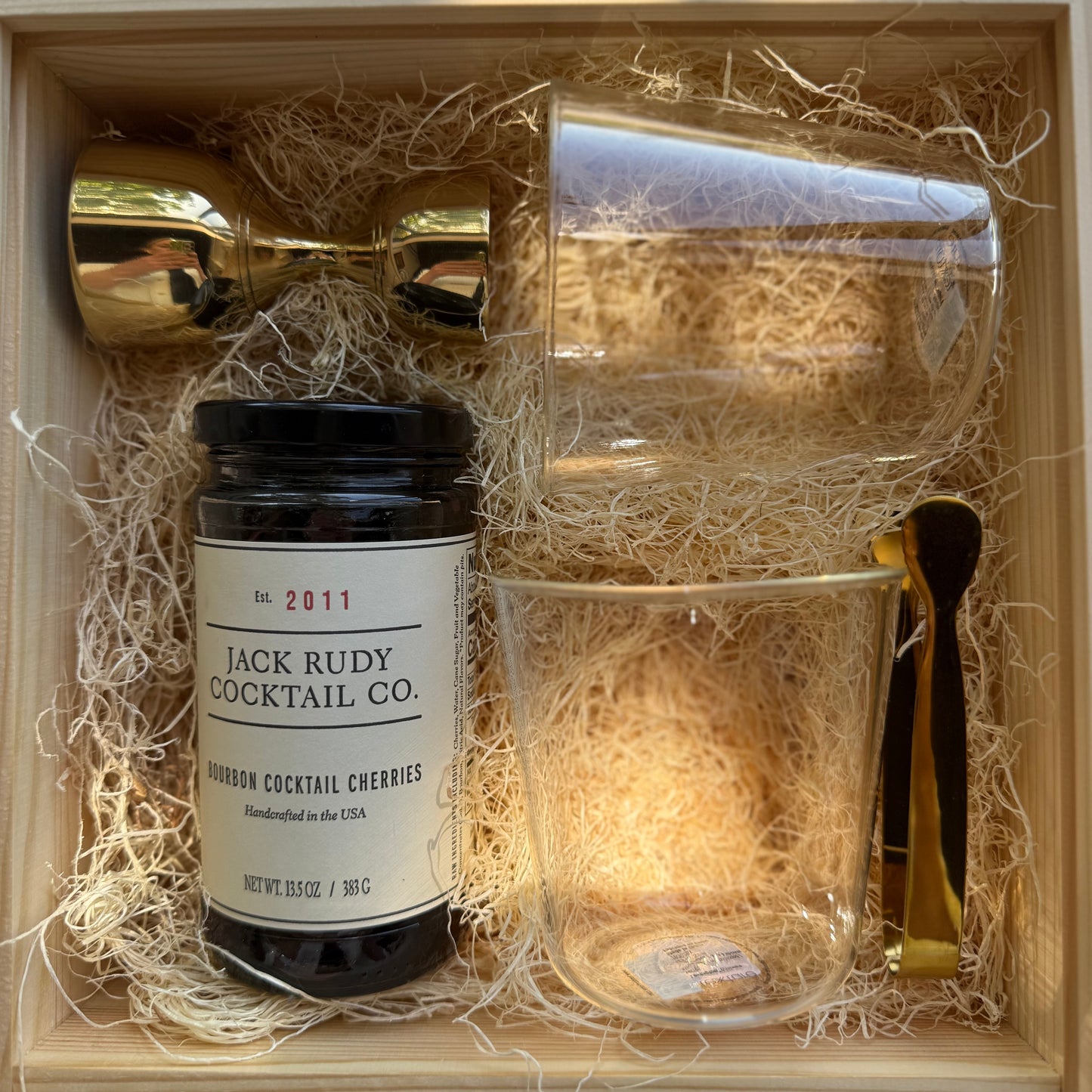 Gift set with Jack Rudy cocktail cherries, glasses, and a spoon in a wooden box.
