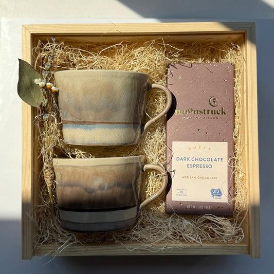 Two ceramic mugs and a chocolate bar in a gift box with moonstruck chocolate packaging.