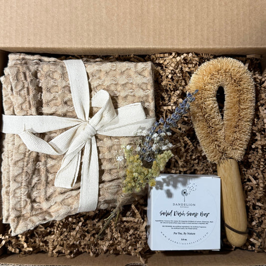 Box containing a stack of natural towels, a brush, and a bar of soap with a label.