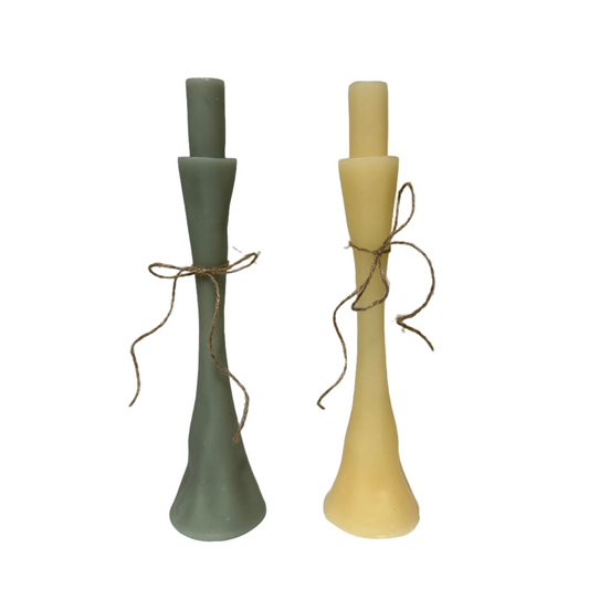 Two candlesticks, one green and one yellow, tied with twine on a white surface.