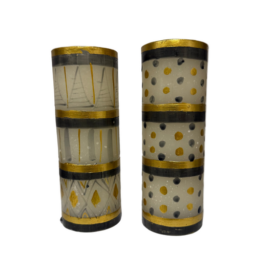 Two cylindrical decorative items with gold and black patterns on a white surface.