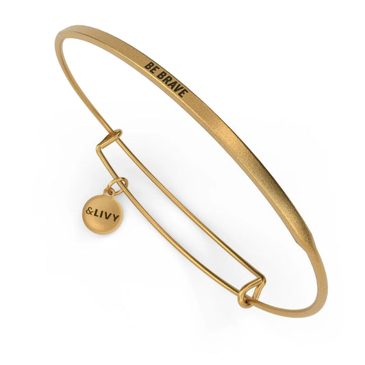 Gold bangle with 'BE BRAVE' engraving and a small round charm on a white background