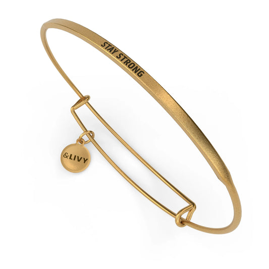 Gold bangle with 'Stay Strong' engraving and a small round tag on a white background
