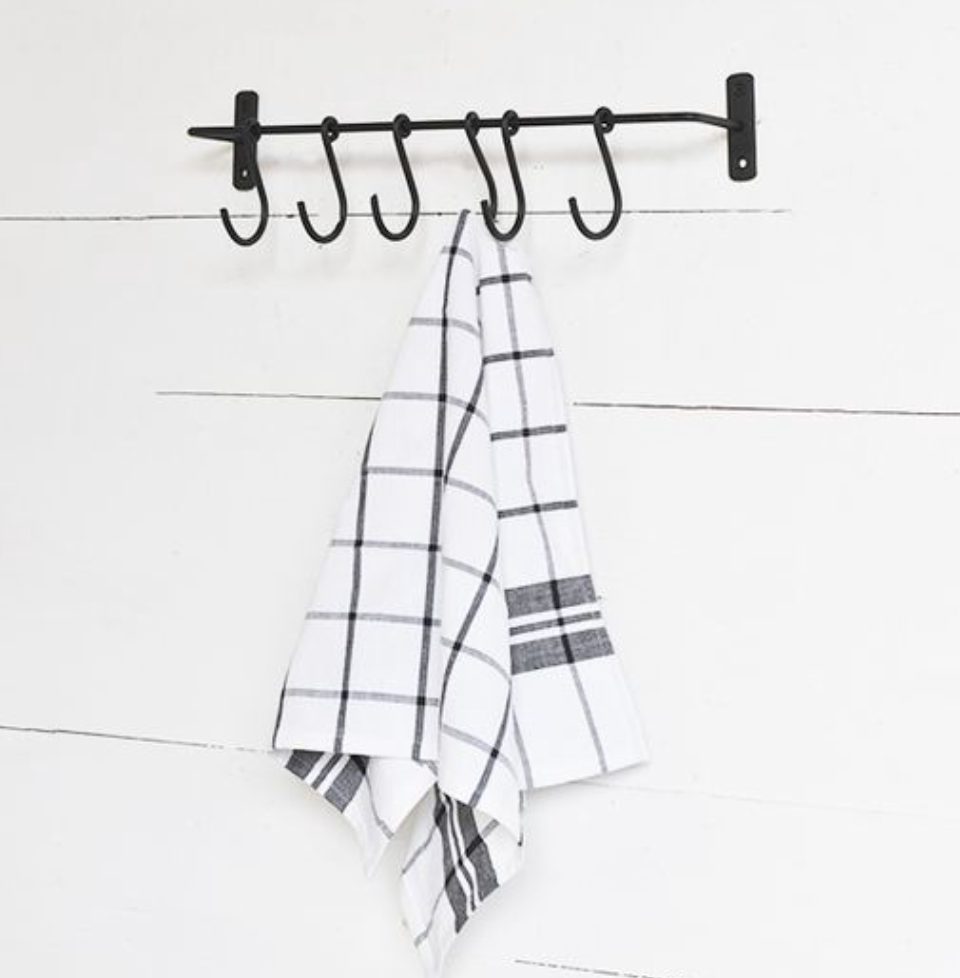 Black metal hook rack with plaid towels on a white wooden background