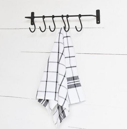 Black metal hook rack with plaid towels on a white wooden background