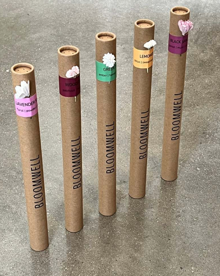 Set of brown cardboard tubes with Bloominell branding and flower labels on a concrete surface.