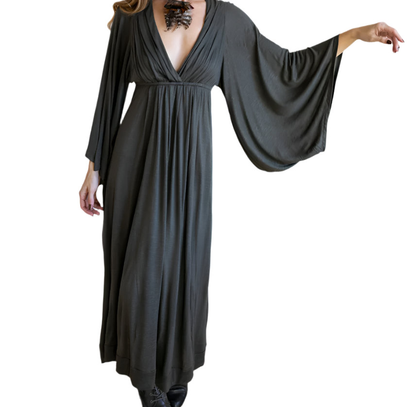 Woman wearing a long, dark gray dress with wide sleeves against a white wall.