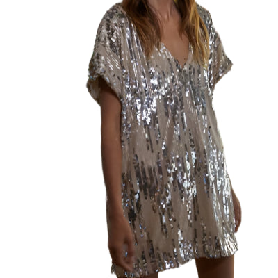 Woman wearing a silver sequin dress in an indoor setting with a wooden wall and books.