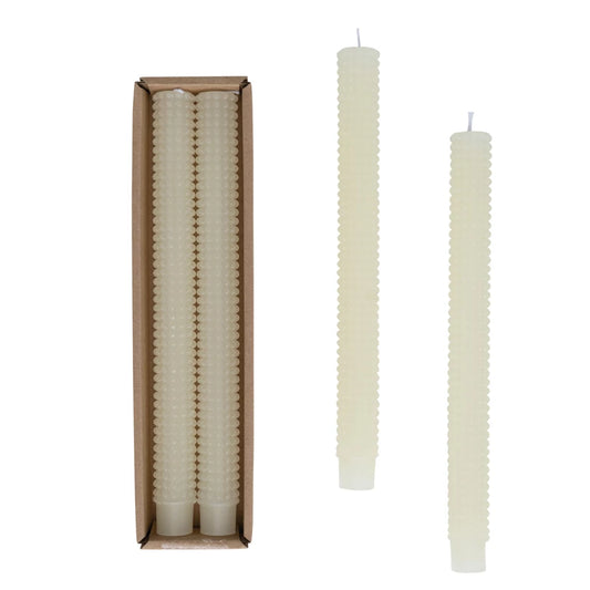 Set of white textured candles with one candle outside its packaging on a white background