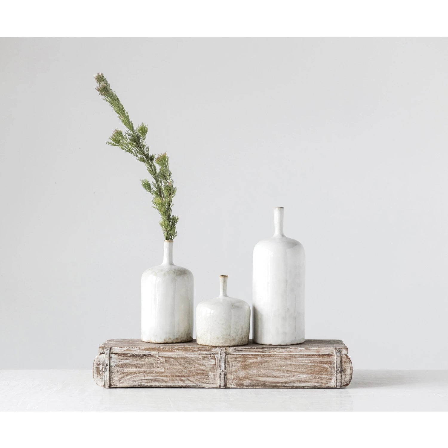 Three white ceramic bottles with a branch on a wooden block against a light gray background